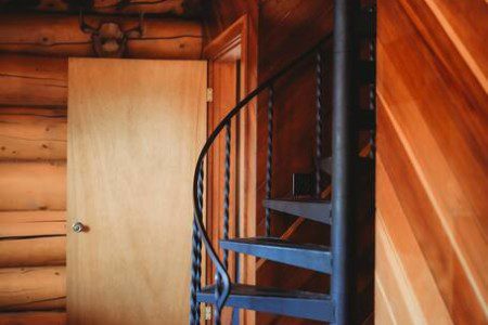 Black spiral staircase in a log cabin-style Fairbanks treehouse rental with wood walls and cozy design