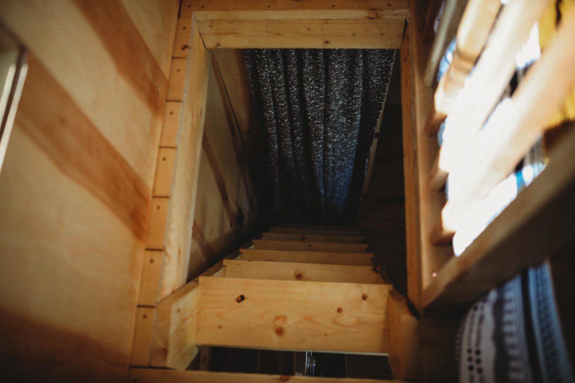 Rustic wooden staircase leading to a loft area, framed with pine walls and patterned curtains in a Fairbanks Alaska treehouse