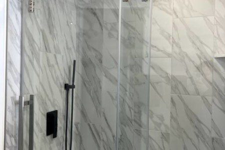 Glass-enclosed shower with marble-style tile in a modern Fairbanks treehouse bathroom