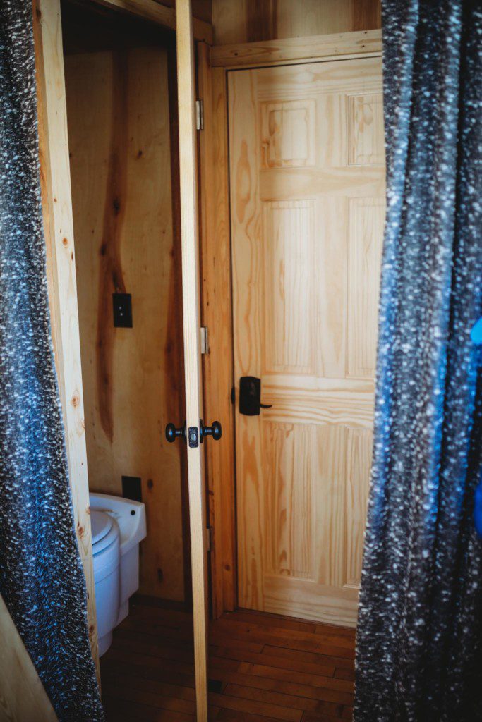 Wood-paneled bathroom with curtain doorway and view of toilet in a cozy Fairbanks Alaska treehouse rental