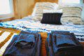 Folded dark towels on a wooden bench in front of a cozy bed with patterned pillows in a Fairbanks Alaska treehouse rental