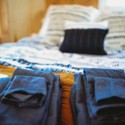 Folded dark towels on a wooden bench in front of a cozy bed with patterned pillows in a Fairbanks Alaska treehouse rental