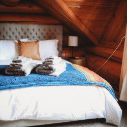 Comfortable bed with colorful blanket and folded towels in a wood-paneled loft in Fairbanks Alaska