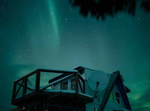 Treehouse-style home under glowing aurora borealis in Fairbanks Alaska night sky