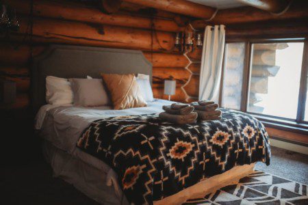 Cozy bedroom with log walls, patterned blanket, and large windows in a Fairbanks Alaska treehouse rental