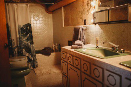 Rustic bathroom with green sink, patterned cabinetry, shower, and wood accents in a Fairbanks Alaska treehouse rental