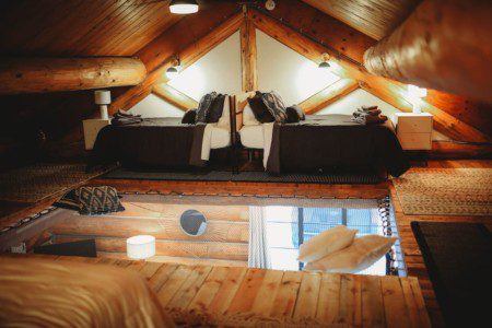 Wood-beamed loft with twin beds and rustic decor in a Fairbanks Alaska treehouse rental