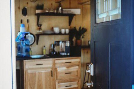 Open front door revealing cozy kitchenette with wooden cabinets and black countertop in a Fairbanks Alaska treehouse rental