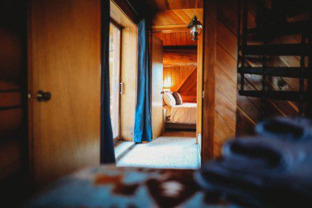 View through wooden hallway into a warmly lit bedroom in a Fairbanks Alaska cabin