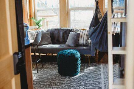 Cozy treehouse living room with couch, pouf, hammock chair, and large windows in Fairbanks Alaska