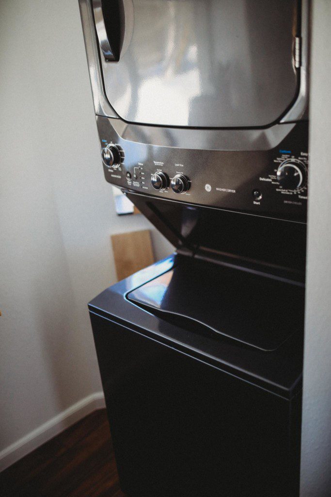 Black stacked washer and dryer unit inside a Fairbanks Alaska lodge, offering convenience for long stays