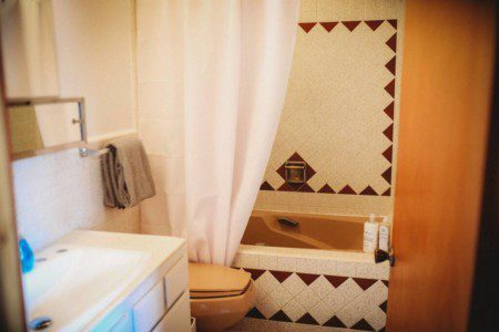 Rustic bathroom with brown tile accents, soaking tub, and white vanity inside a Fairbanks Alaska treehouse rental