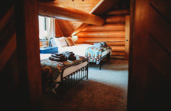 Neatly folded gray towels on a white bed with striped pillow in a bright Fairbanks Alaska treehouse rental bedroom