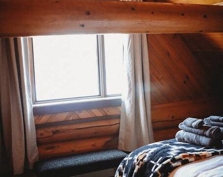 Bottle of champagne and glasses on bed with patterned blanket in cozy Fairbanks treehouse rental