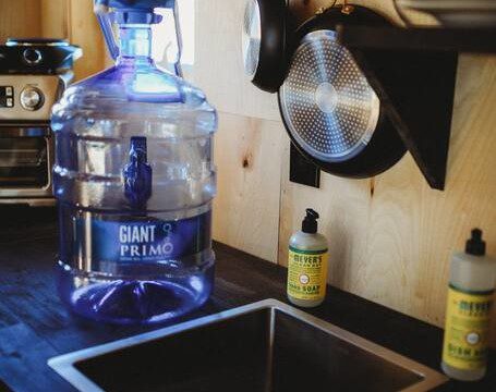 Compact treehouse kitchen with water dispenser, hanging pans, and soap near small sink in Fairbanks Alaska