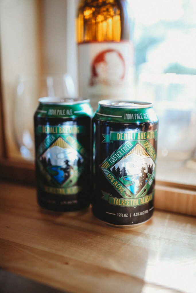 Two cans of local craft beer on a wooden counter inside a cozy Alaska adventure lodge near Fairbanks