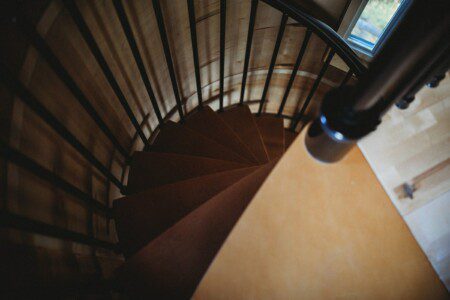 Top-down view of a wooden spiral staircase with black railing in a cozy Fairbanks Alaska treehouse rental