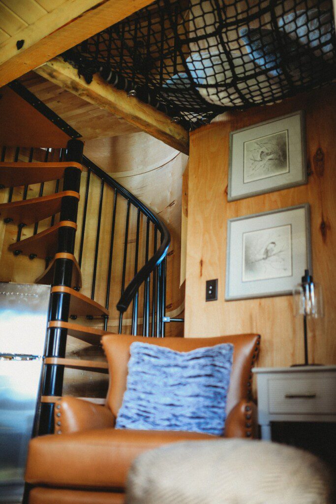 Cozy interior of Fairbanks Alaska treehouse with spiral staircase, leather chair, and loft netting