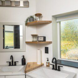 Modern double-sink bathroom with black fixtures and wood shelving in a Fairbanks Alaska treehouse rental.