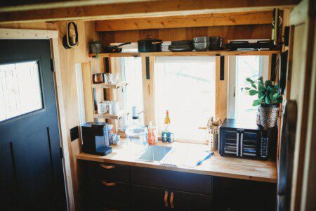 Wood and black kitchen with large windows, coffee setup, and natural light in a Fairbanks Alaska treehouse rental