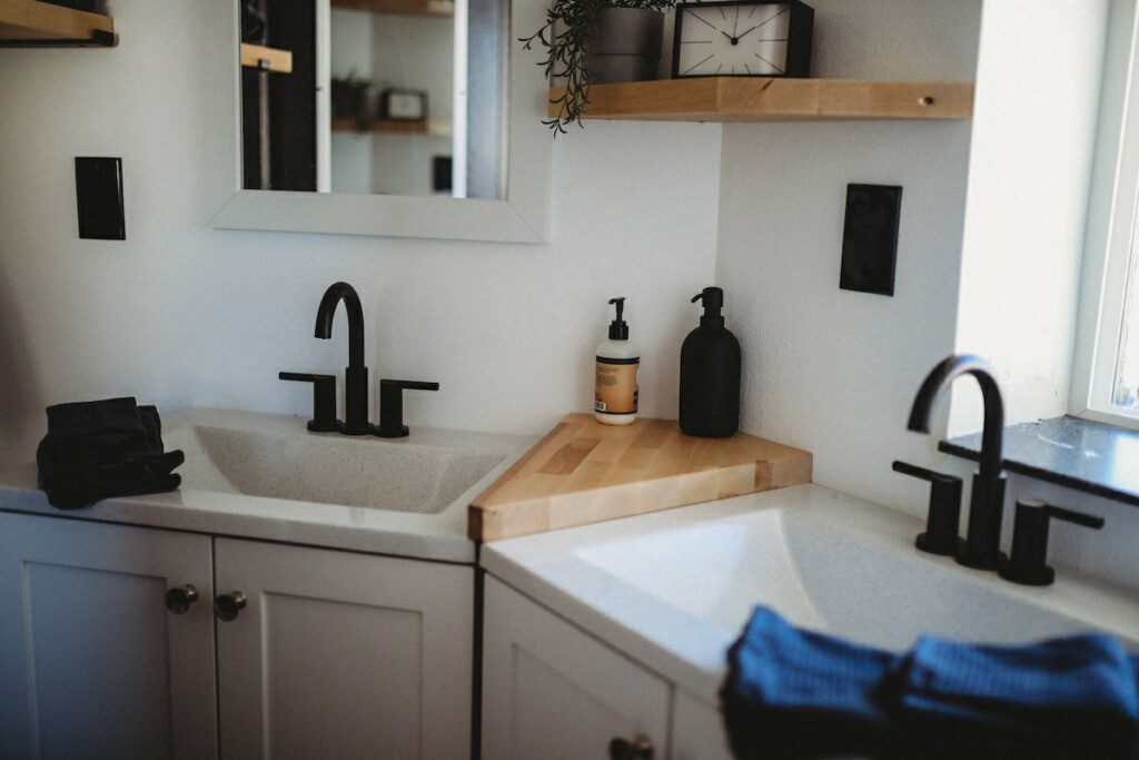 Modern double-sink bathroom with black fixtures and wood shelving in a Fairbanks Alaska treehouse rental.