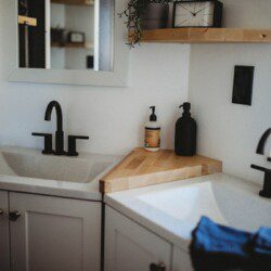 Modern double-sink bathroom with black fixtures and wood shelving in a Fairbanks Alaska treehouse rental.