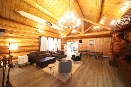 Spacious log cabin living room with wooden beams, cozy seating, and bear carving in Fairbanks, Alaska.
