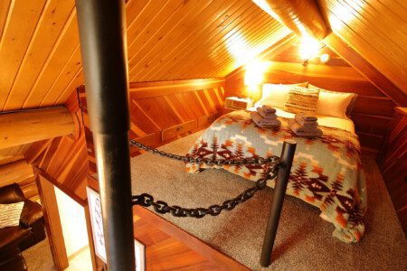 Rustic cabin bedroom with tribal blanket, soft lighting, and wooden walls in a Fairbanks, Alaska treehouse rental.