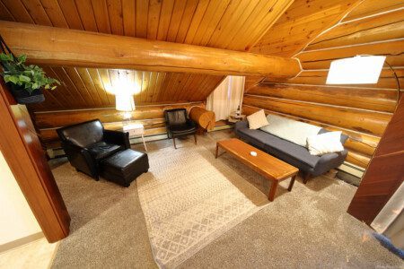 Warm log cabin living room in Fairbanks Alaska with wooden interior, couch, and spiral staircase