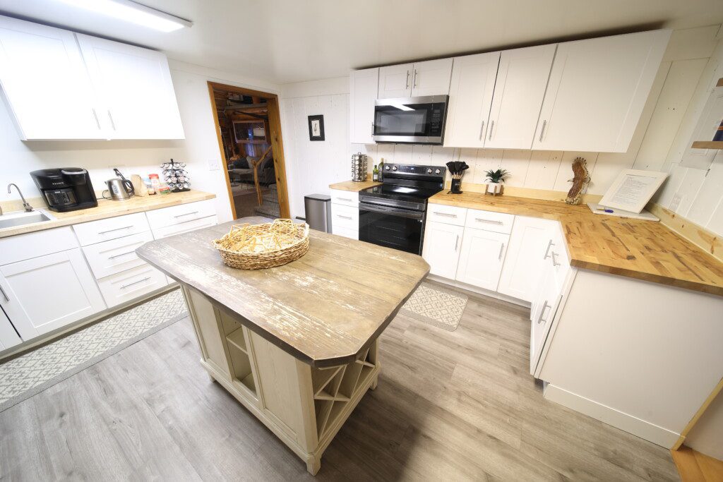 Bright rustic kitchen with white cabinets, wood countertops, and central island in a Fairbanks adventure lodge