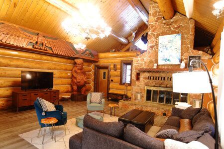 Spacious log cabin living room with wooden beams, cozy seating, and bear carving in Fairbanks, Alaska.