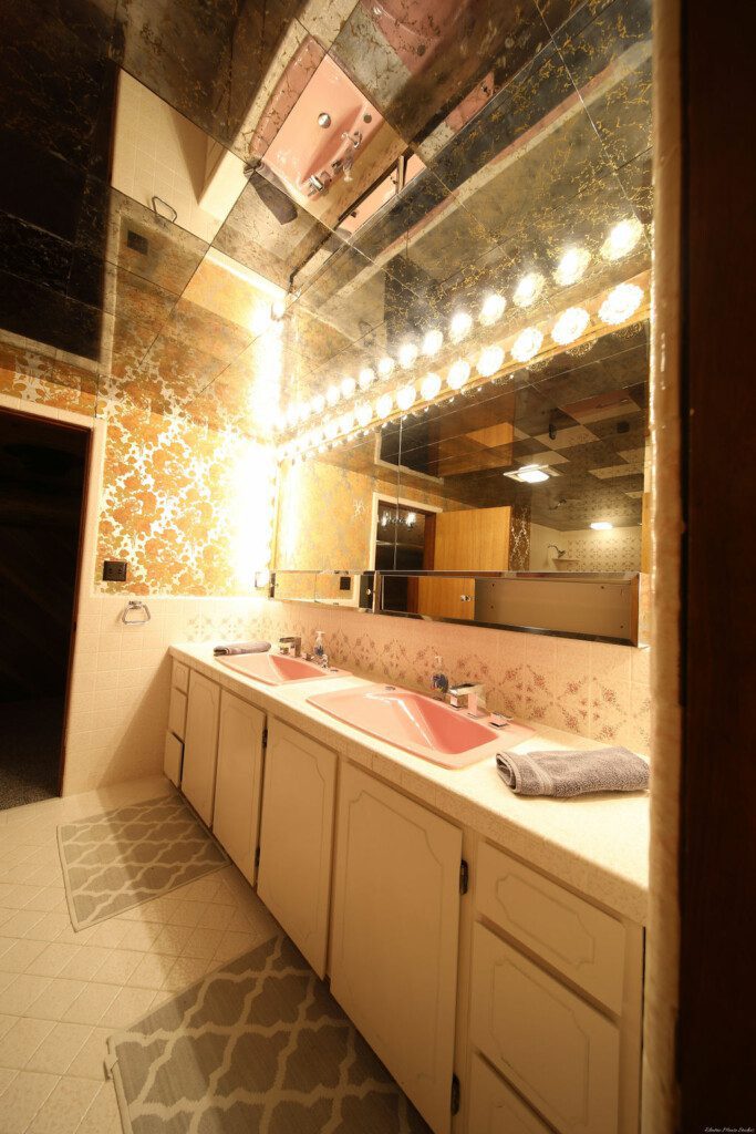 Retro-style bathroom with dual pink sinks, large mirrors, and warm vanity lighting in a Fairbanks Alaska lodge
