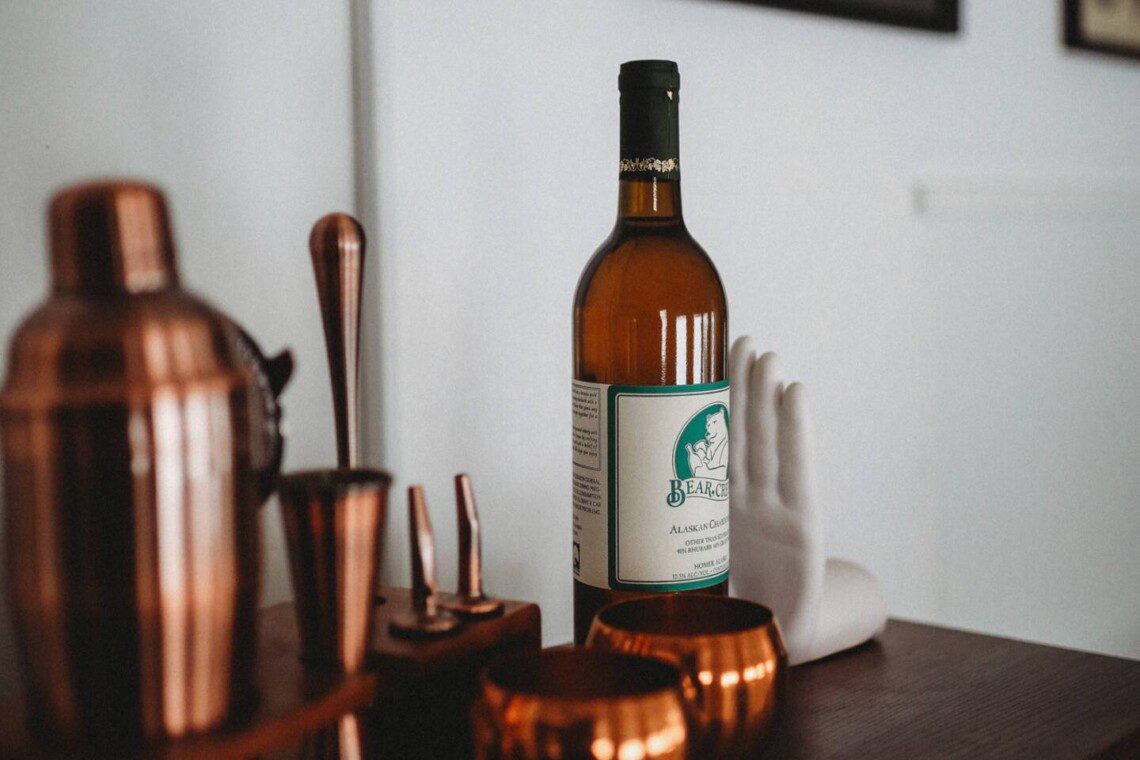 Bottle of alcohol with copper bar tools and mugs on a wooden counter in a Fairbanks Alaska lodge rental
