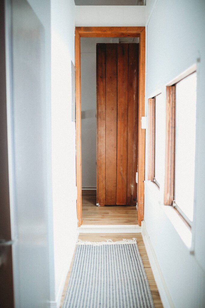 Narrow hallway with wooden door, white walls, and natural light in a Fairbanks Alaska adventure lodge
