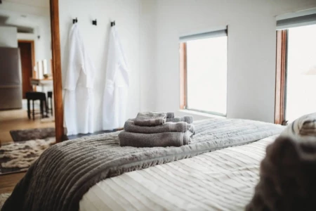 Stacked towels on a bed with plush blankets and robes hanging in a modern Fairbanks Alaska lodge