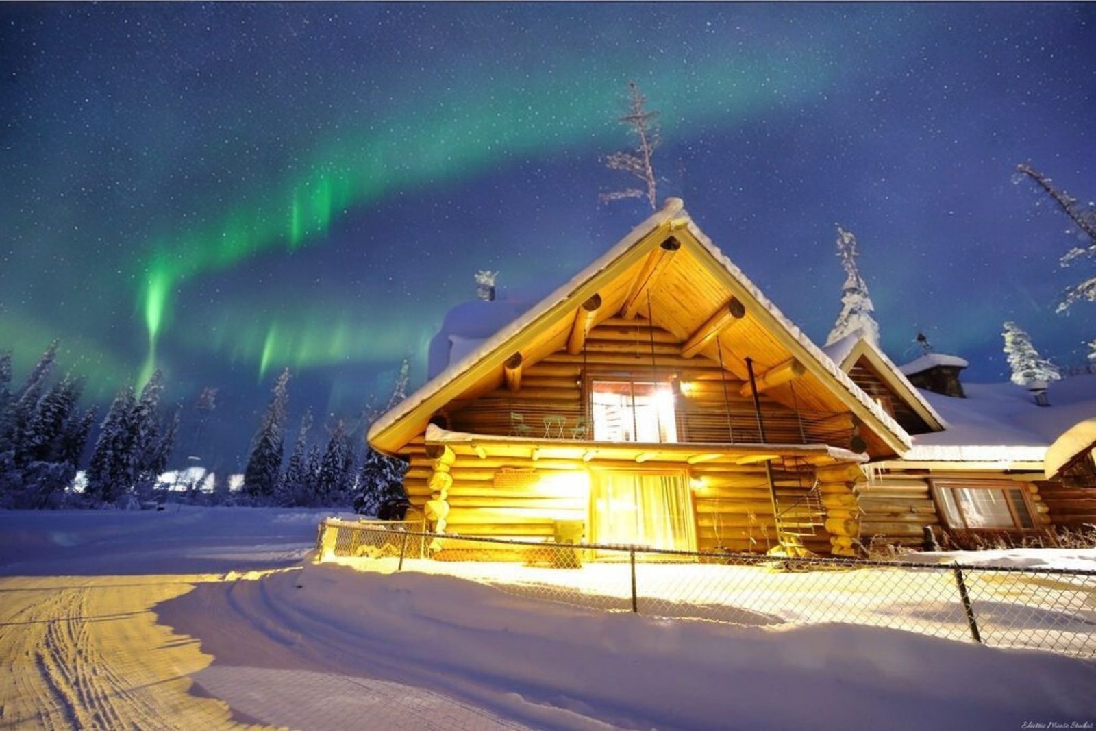 Log cabin in snowy Fairbanks lit under green aurora at an Alaska adventure lodge.