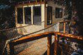 Couple standing on a snowy wooden treehouse deck surrounded by pine trees in Fairbanks Alaska