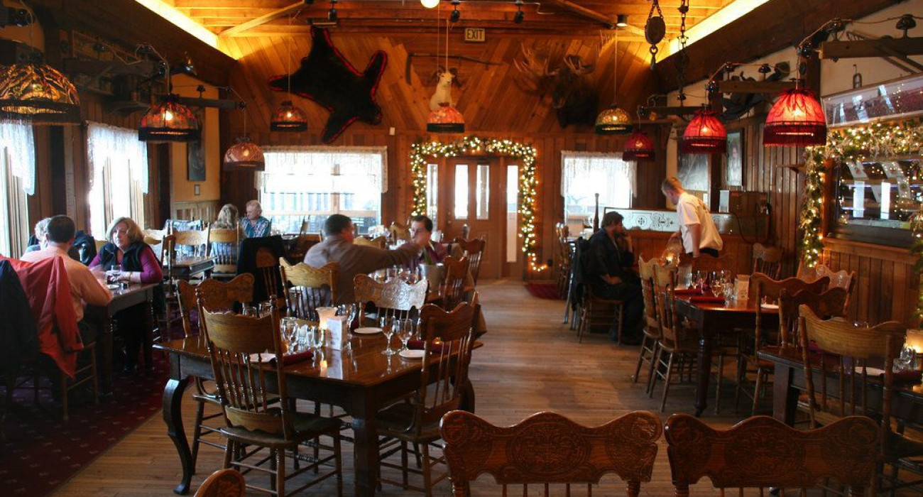 Rustic wood interior of an Alaskan lodge-style restaurant with guests dining under warm lighting