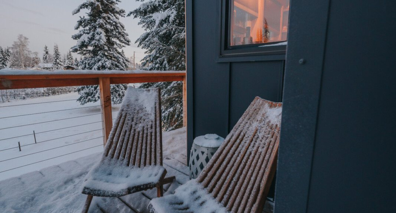 Two wooden chairs on a snow-covered balcony outside a modern treehouse rental in Fairbanks Alaska